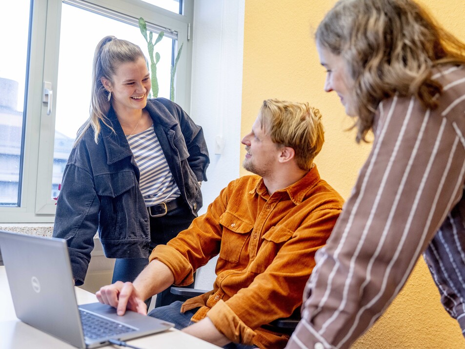 Drei Mitarbeiter lächelnd vor Laptop