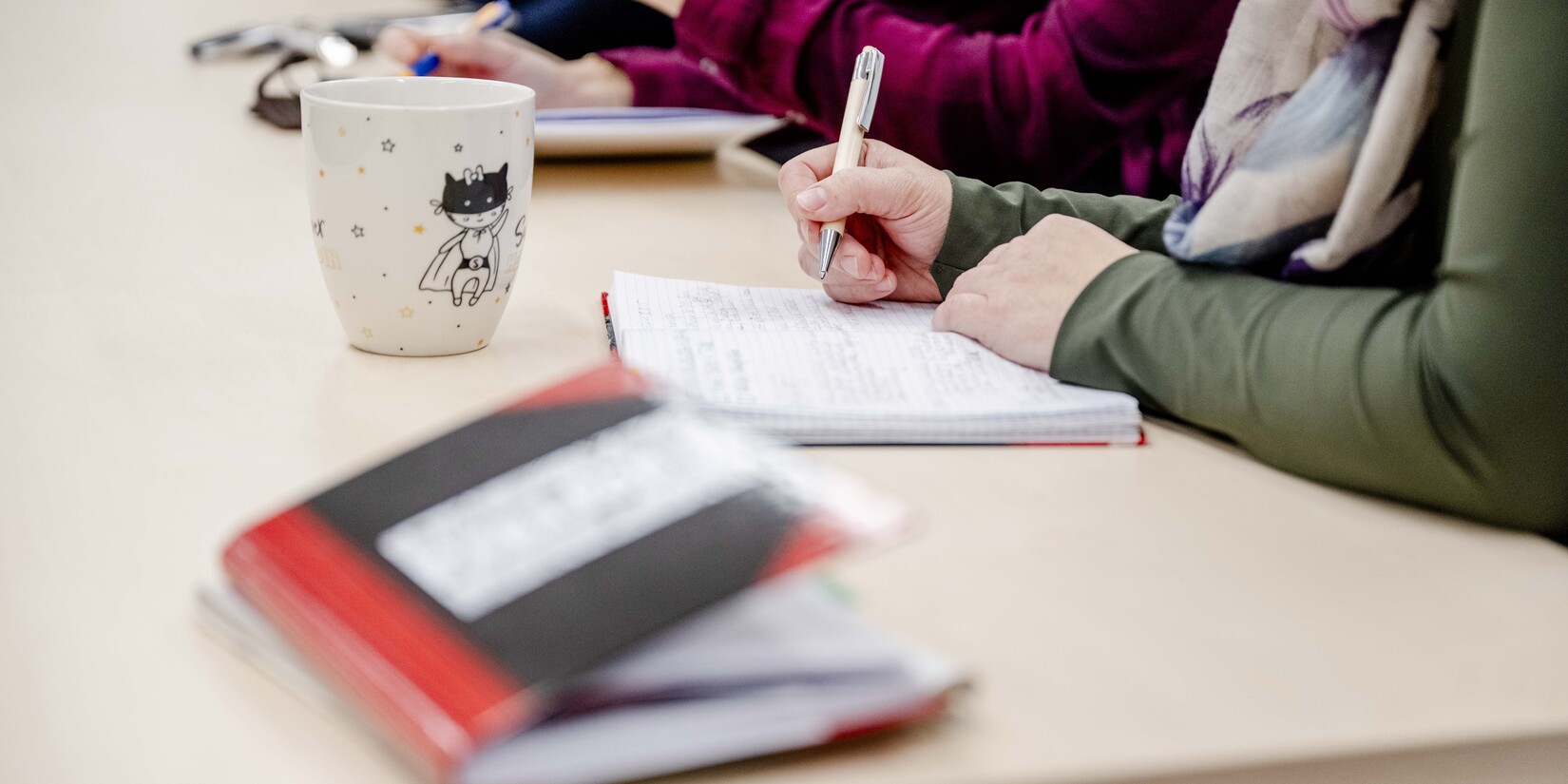 Tisch in Meeting-Situation, Notizbuch, Person nimmt Notizen